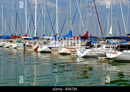 Sailboats on a dock at a marina with reflections on water on a sunny day with beautiful blue green water and partly cloudy skies Stock Photo