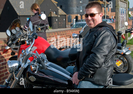 A Harley-Davidson rider wearing a black leather jacket and dark sunglasses, looking at the camera, Rye, East Sussex, England, UK Stock Photo