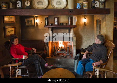 Two women sitting by an open fire in the Bushmills Inn, Bushmills, County Antrim, Northern Ireland Stock Photo