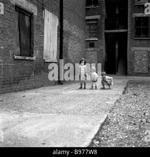 1950s, three young children play on their own at the back of some boarded-up abandoned slum housing or tenements, East End, London, England, UK. Stock Photo