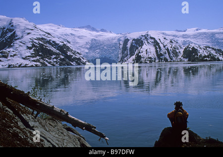 a sea kayaker sitting on a rock viewing Blackstone Bay s glaciers on a calm evening in the Prince William Sound Alaska Stock Photo