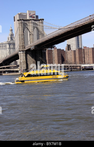 Water taxi ferry boat travels north on the East River under the Brooklyn Bridge, New York City, USA Stock Photo