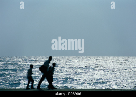 Man walking with two sons, silhouetted against ocean Stock Photo