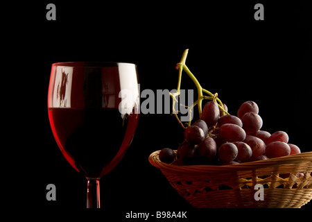 A glass of red wine and a basket of red grapes. Stock Photo