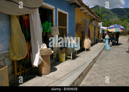 Street in town. Rows of terraced houses.  Shops. Doorways. Goods on display. EL VALLE. ISLA MARGARITA. VENEZUELA. Stock Photo