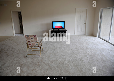 Flat Panel LCD TV Television sits alone in empty living room with folding chair Stock Photo