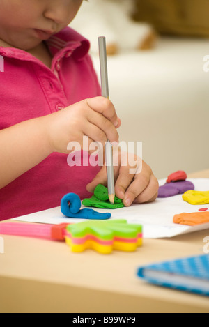 Little girl shaping colorful clay with pencil, cropped view Stock Photo