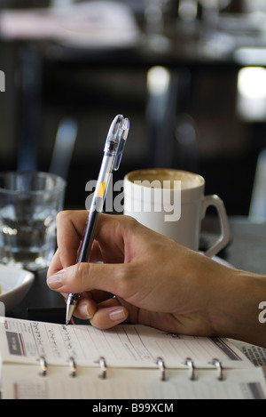 Woman sitting in cafe, writing in agenda, cropped view of hand Stock Photo