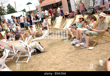 Festival goers relax and enjoy the Sunday papers in deck chairs. Stock Photo