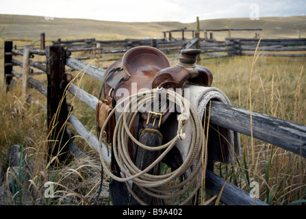Cowboy's Horse Saddle and Lasso hanging over a Rail Fence around a Ranchland Corral Stock Photo