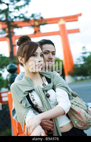 Young couple leaning against railing together, traditional Japanese Torii gate in background Stock Photo