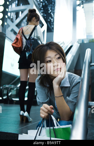 Young shopper sitting on steps, hand under chin Stock Photo
