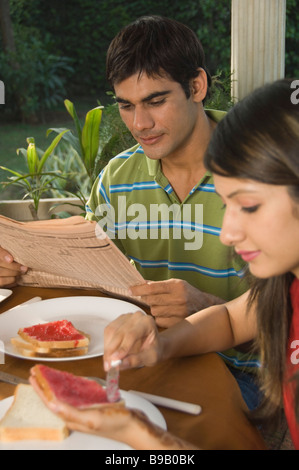 Woman having breakfast while a man reading a newspaper Stock Photo