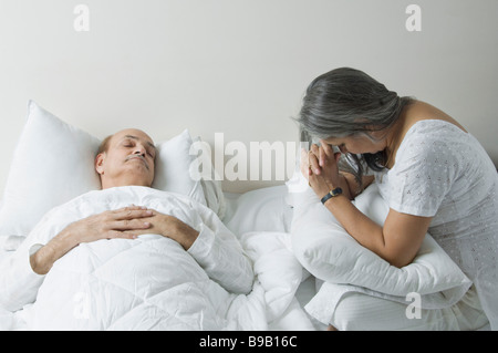 Ill man lying on the bed with his worried wife sitting beside him Stock Photo