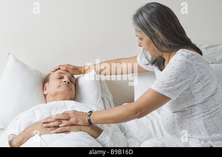 Ill man lying on the bed with his wife checking his temperature Stock Photo