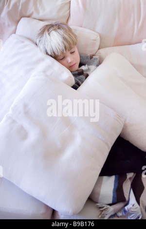 Exhausted three year old boy sleeping on sofa surrounded by cushions Stock Photo