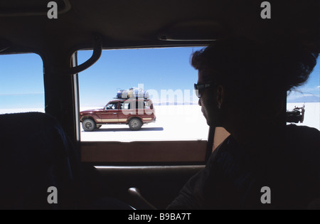 A tourist looks out the window to another truck traveling across the Salar de Uyuni Stock Photo