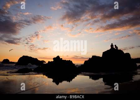 Couple watching the sunset on silhouetted rocks at Manuel Antonio National Park in Costa Rica. Stock Photo