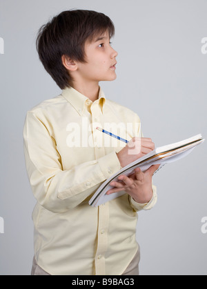 Asian American boy takes notes in his notebook while looking into ...