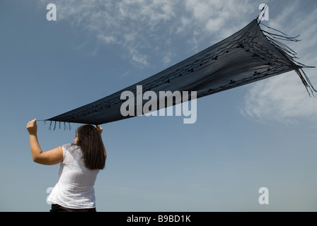 Woman waving with a black scarf against a blue sky Stock Photo