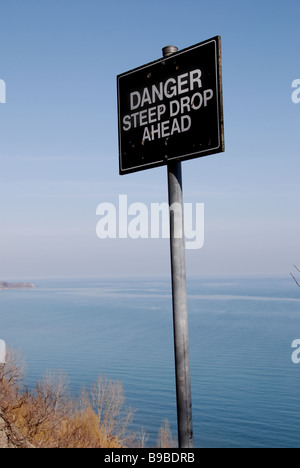 A danger sign warning of a steep drop ahead on the edge of a cliff. Stock Photo