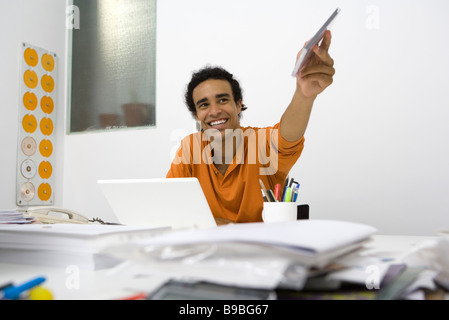 Young man sitting at messy desk, holding out CD case Stock Photo