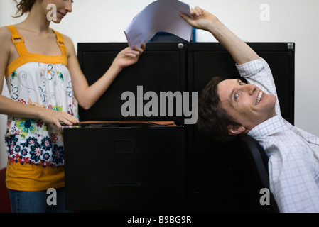 Man leaning back in chair, handing document to woman Stock Photo