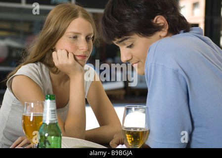Young couple sitting at outdoor cafe, looking down at book Stock Photo