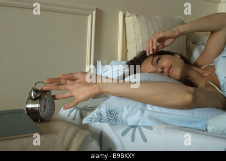 Young woman lying in bed, silencing alarm clock Stock Photo