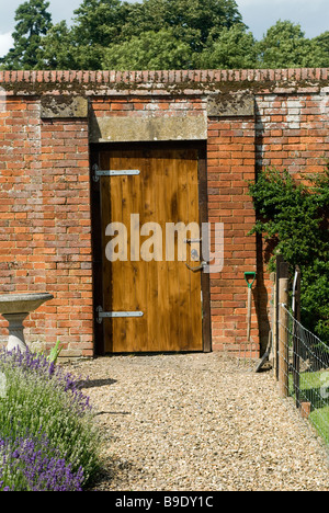 Beautiful wooden door at the entrance to a walled garden with the gardeners tools propped up on the path outside Stock Photo