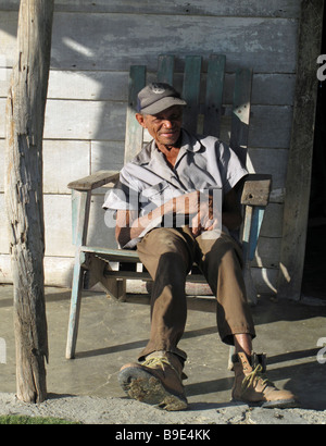 older working man sitting in wooden chair  relaxing after work on sunny deck of simple wooden house Stock Photo