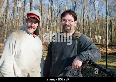two smiling workman builders contractors partners repairing chain link fence outdoors in winter Stock Photo