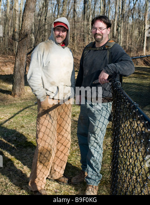 two smiling workman builders contractors partners repairing chain link fence outdoors in winter Stock Photo