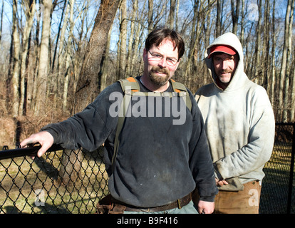 two smiling workman builders contractors partners repairing chain link fence outdoors in winter Stock Photo