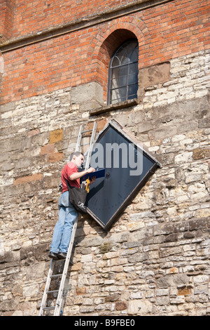 Man on ladder examining a church clock. Model release may be available on request. Stock Photo