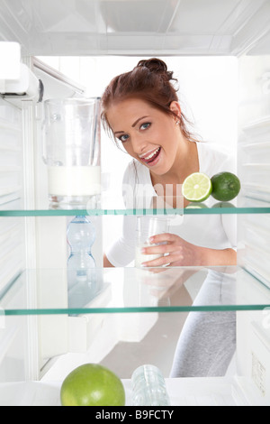 Portrait of young woman putting milkglass in refrigerator and smiling Stock Photo