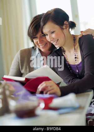 Woman and her daughter reading book at table Stock Photo