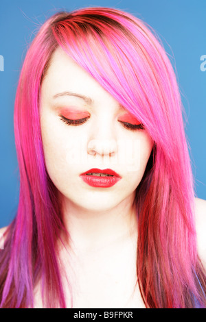 Young teen with bright pink hair red lips and eye shadow looking down to the ground. Stock Photo