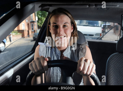 A nervous but determined female learner driver sits gripping the steering wheel of a car Stock Photo