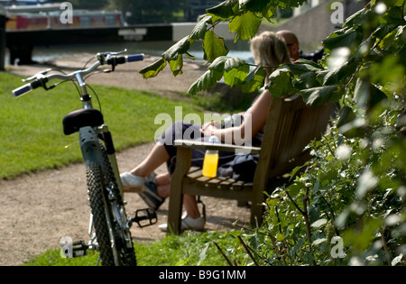 Couple sat on bench on summers day with bike in foreground Stock Photo