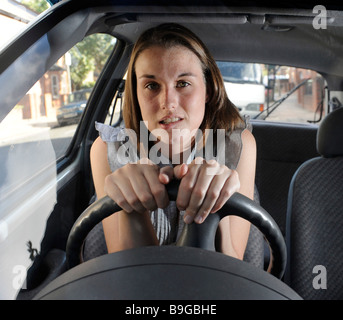 A nervous female learner driver sits anxiously gripping the steering wheel of a car Stock Photo