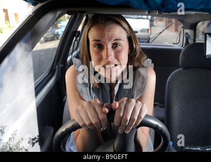 A nervous female learner driver sits anxiously gripping the steering wheel of a car with white knuckles Stock Photo