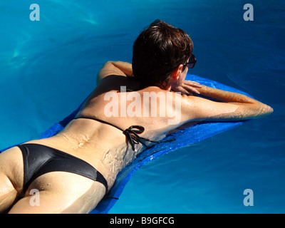 A young woman lying on a mat in a swimming pool. Stock Photo