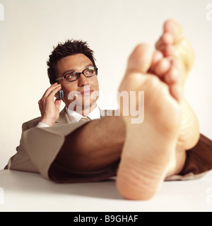 Managers barefoot feet puts up cell phone telephones series desk table people man 30-40 years sitting  leans back feet Stock Photo