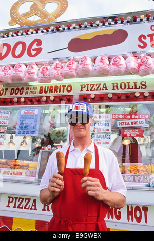 A server at a corn dog stand at the Mid-State Fair in Paso Robles, California displays two corn dogs, one in each hand. Stock Photo