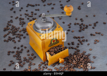 Antique wooden coffee grinder surrounded by many scattered coffee beans on a stone surface Stock Photo