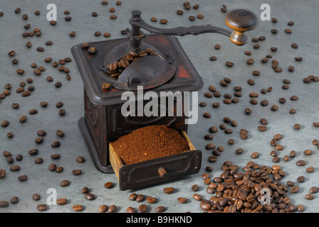 Antique metal coffee mill with a drawer full of ground coffee, standing amidst scattered coffee beans Stock Photo