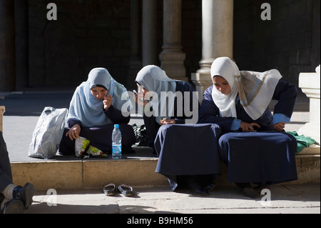 Three girls wearing traditional clothes, sitting, phoning, listening, mobile phone, An-Nasir Muhammad Mosque, inner yard, citad Stock Photo