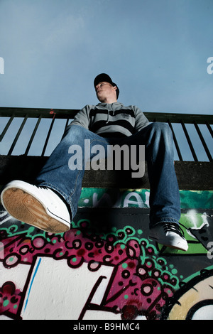 Young man sitting on a graffiti sprayed wall Stock Photo