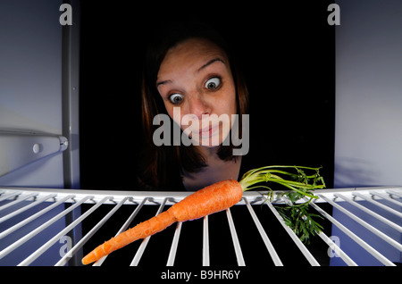Young woman regarding a single carrot in an empty refrigerator Stock Photo